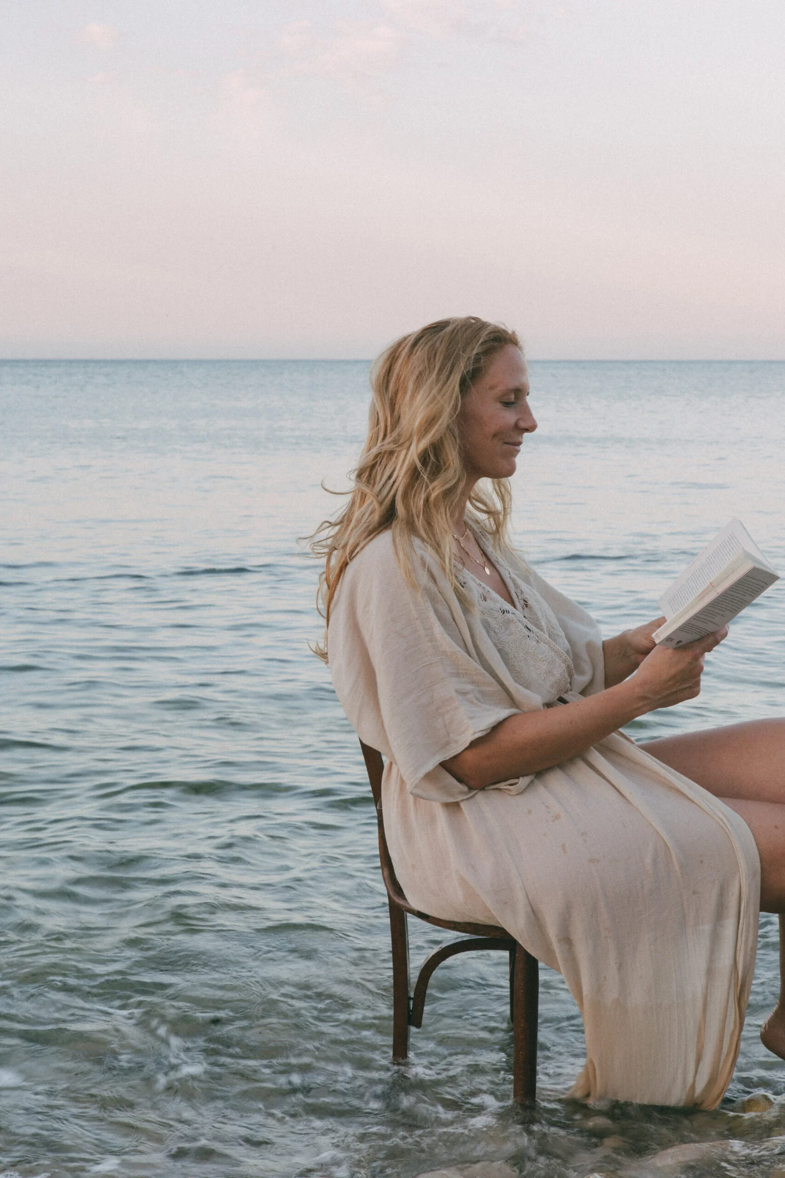 Mujer sentada junto al mar leyendo un libro